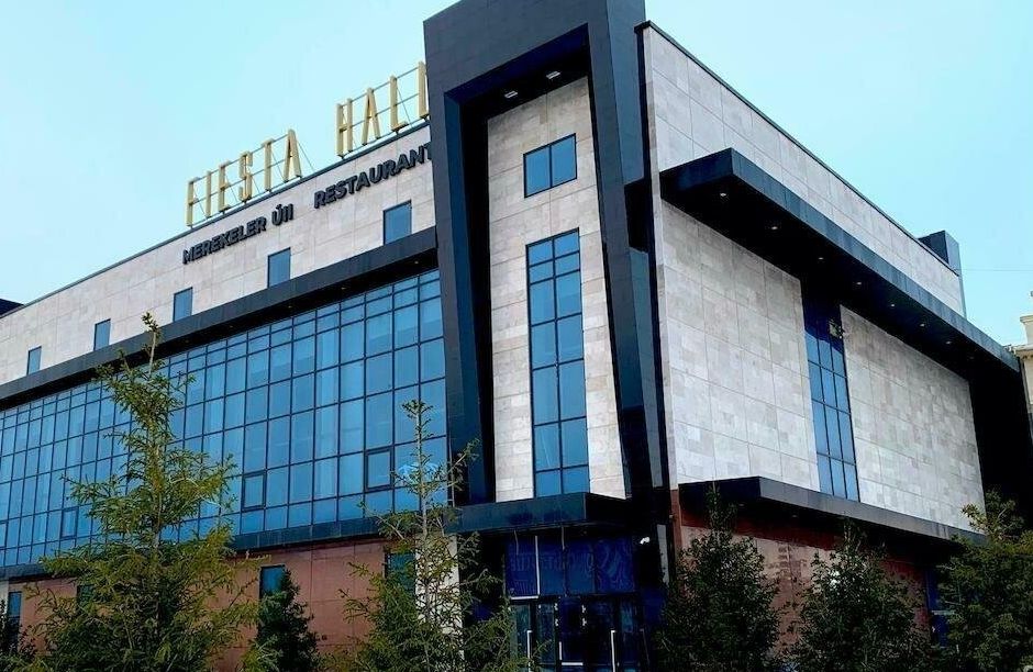 Здание FIESTA HALL: стекло и светлый камень, золотая вывеска на крыше